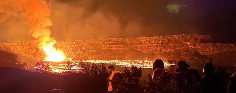 a group of people standing at edge of Halema'uma'u Crater watching eruption fountain