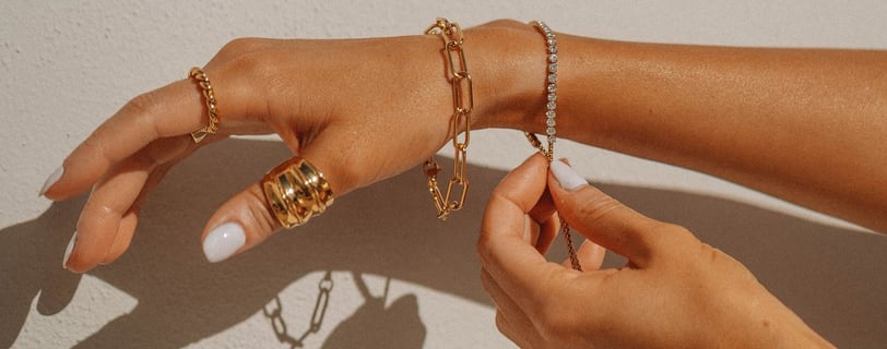 Foto de mão com pulseiras e anéis em dourado.