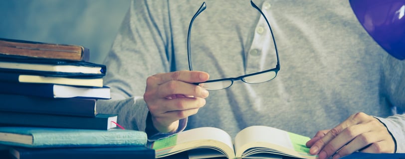 a man is sitting at a desk with a book and glasses