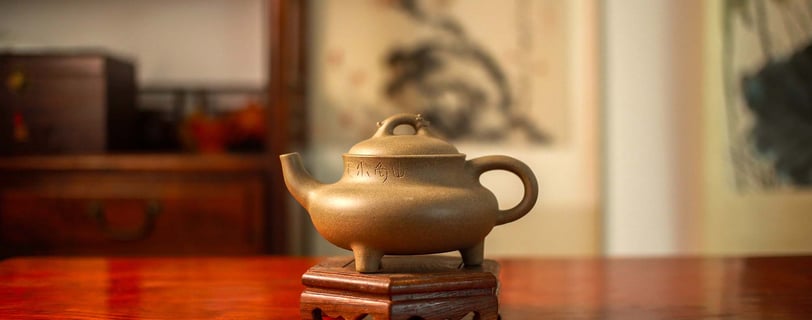 A clay-colored Yixing teapot is placed on a wooden stand