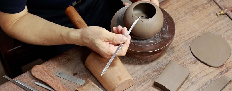 person holding a sharp knife to smooth the surface of a teapot