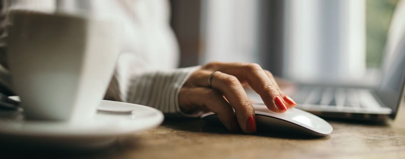 a woman at a laptop with hand on a mouse and a coffee mug on table