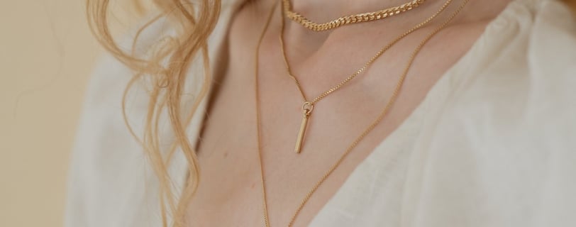 Foto do pescoço de uma mulher utilizando três colares diferentes em dourado.