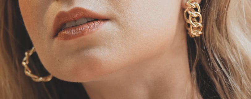 Foto de metade do rosto de uma mulher mostrando boca e brincos de argola em dourado.