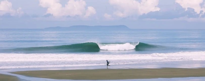 Surfer running on the beach with a perfect wave and an island on the back on a sunny day