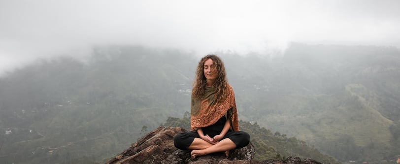 Woman meditating on a mountain top with misty hills in the background