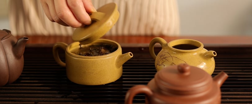 A hand lifting the lid off a teapot, revealing tea inside