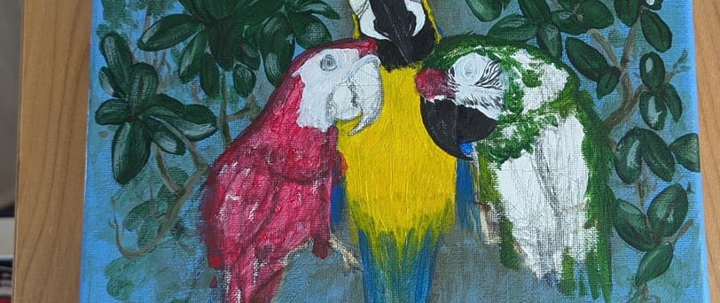 Progress photo of three macaws painting on a wooden easel.