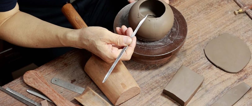 A man holding a long-handled pointed knife, carving the edge of a Yixing teapot