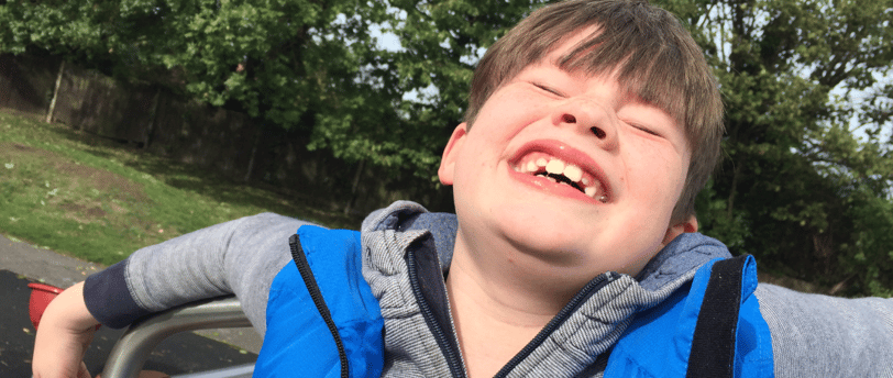 a young boy smiling and laughing while standing in a park. Autista alegre