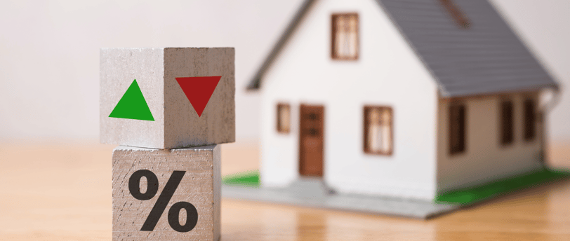 blocks with green and red arrows for interest rates beside tiny house