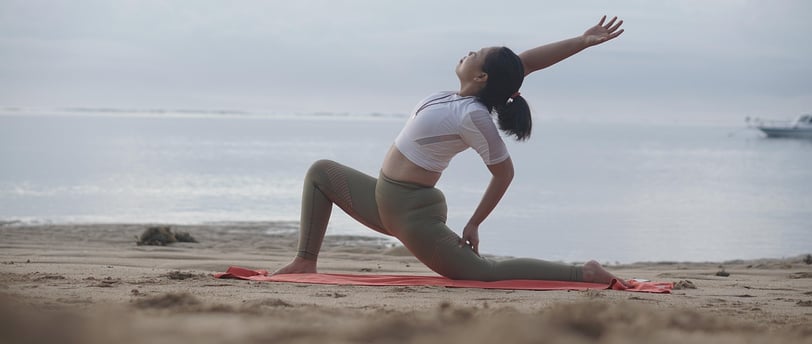 Woman stretching on a beach at sunrise, practicing active recovery with yoga to promote muscle flex