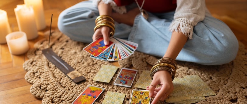 Woman sitting on a rug reading tarot cards, candles and incense on the floor, wearing bracelets