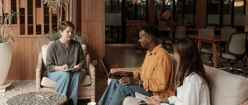 a group of people sitting around a table talking and taking notes