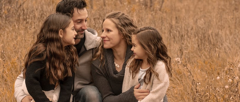 a family photo of three sitting on a field of tall grass