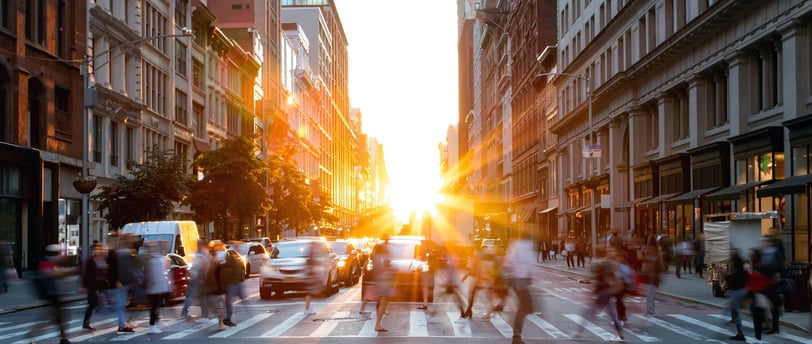a busy city with traffic and pedestrians, and a bright sun setting in the background
