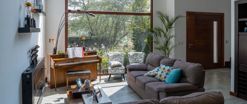 fotografía inmobiliaria quito ecuador tumbaco gran sala de estar con muebles, piano y un gran ventanal con luz natural