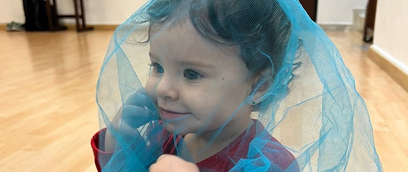 Niña sentada en piso de madera cubierta por una malla azul transparente en Ukelele Jardín Infantil