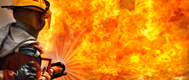 Um bombeiro tenta controlar um grande incêndio com uma potente mangueira de água