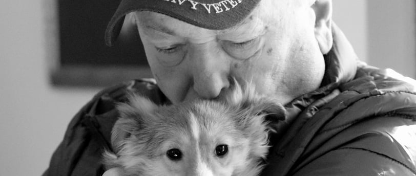 man with navy veteran hat kissing the head of the dog he is holding
