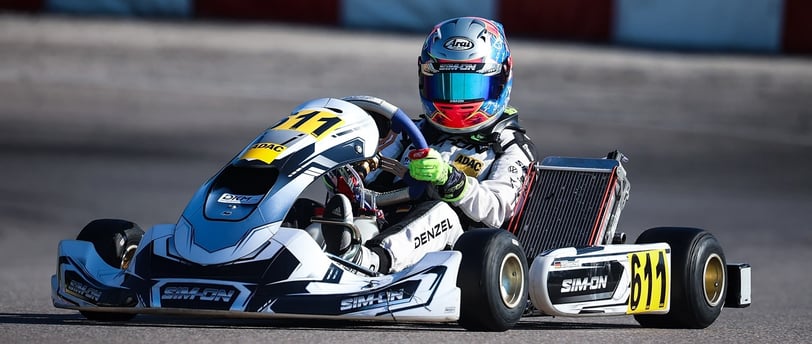 Kart blanc numéro 611 piloté par un compétiteur en combinaison blanche et casque chromé, manœuvrant un virage sur piste.