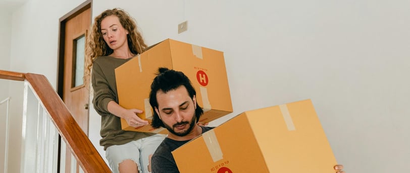 a man and woman moving boxes down stairs