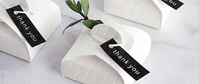 a table with a bunch of small white paper wedding favour boxes