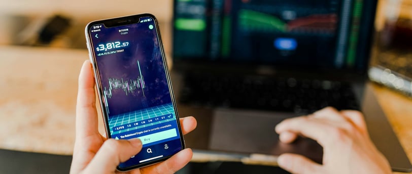 Pessoa analisando gráficos financeiros em um smartphone e um notebook