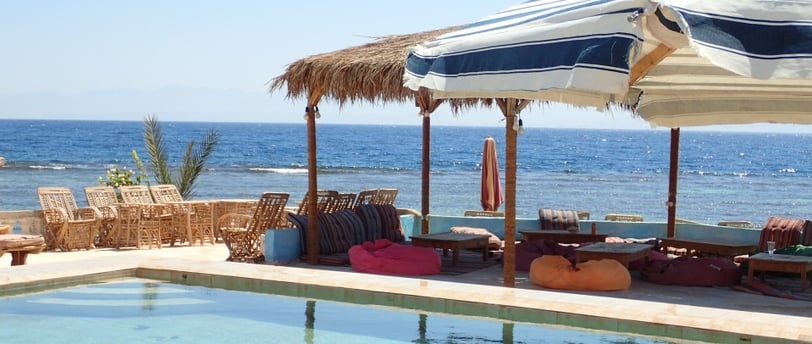 uma piscina na praia com guarda-sóis e cadeiras