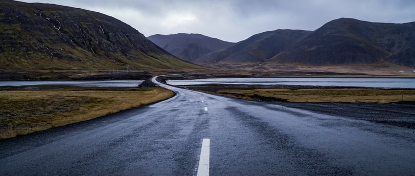 gray concrete road near green mountain under white clouds during daytime