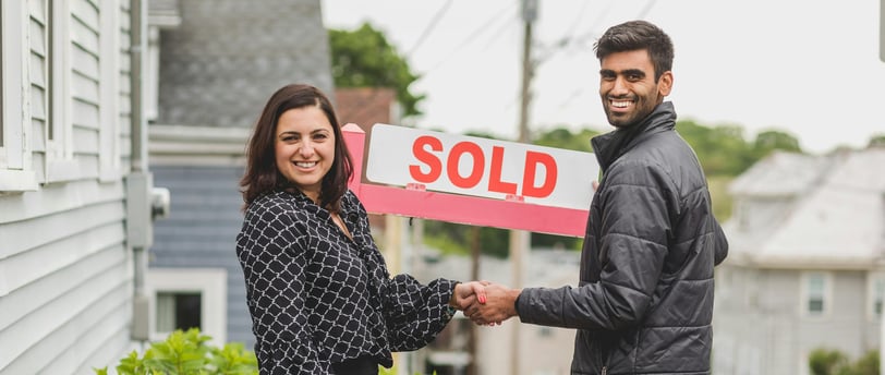 First Time home Buyer in Clagary. A man and woman shaking hands in front of a sold sign