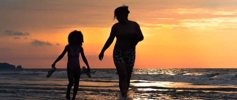 Retrato de una madre y su hija caminando por el agua de la playa en un atardecer