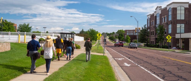 People walking on a sidewalk next to a street with a painted bike lane