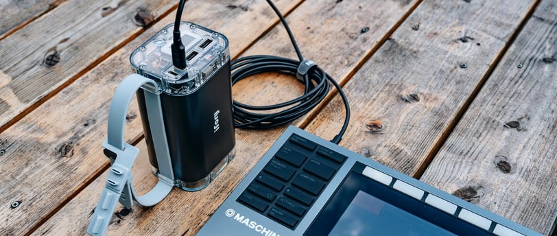 A professional music production setup featuring a Maschine+ controller and connected power source on a wooden table