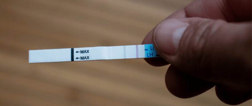 Positive LH ovulation test strip held in hand over wooden background