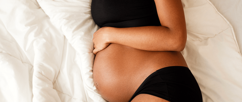 Close-up of pregnant woman lying on bed, holding her bump