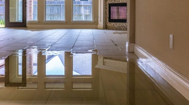 Flooded tiled living room with water damage after a plumbing failure, illustrating the risks of delayed insurance claims.