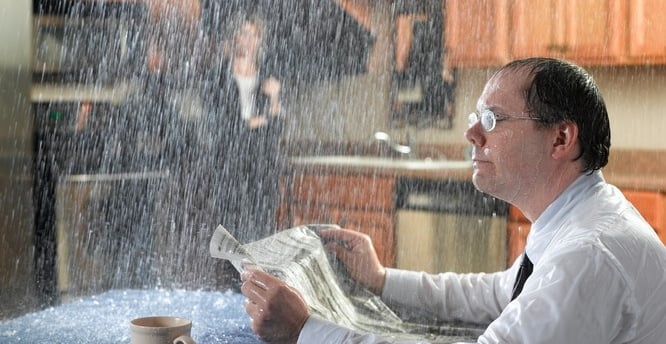 Man overwhelmed by indoor water damage due to a roof leak, highlights the importance of insurance claim assessment