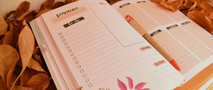 Planner hebdomadaire ouvert sur une page to-do, posé sur un lit de feuilles mortes