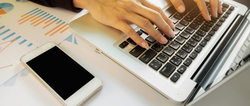 Mulher digitando em um notebook com um celular ao lado