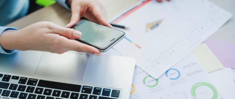 Duas pessoas mexendo em papéis, notebook e celular na mesa