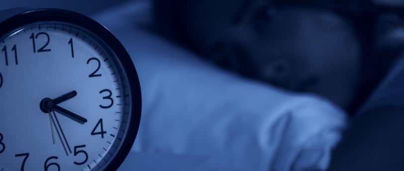 A woman lying in bed, unable to sleep, eyes fixed on her alarm clock