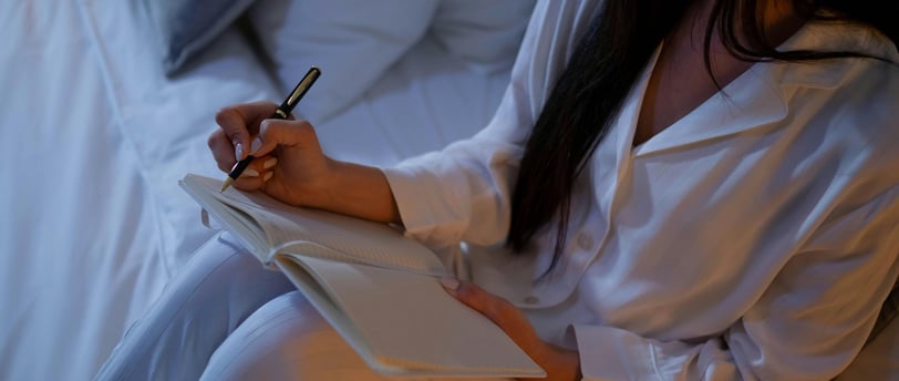 Someone reclining on a bed or couch, jotting down notes
