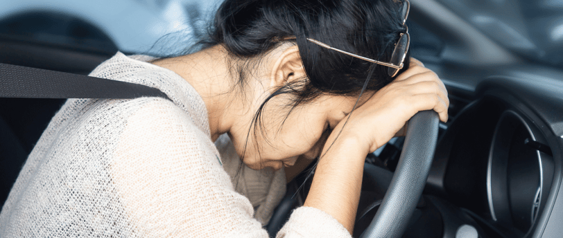 exhausted woman with head and hands resting on steering wheel