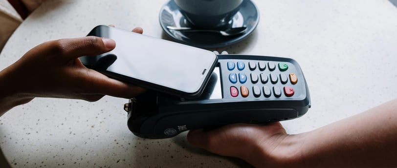 Person using a smartphone for contactless payment on a card reader with a coffee cup.