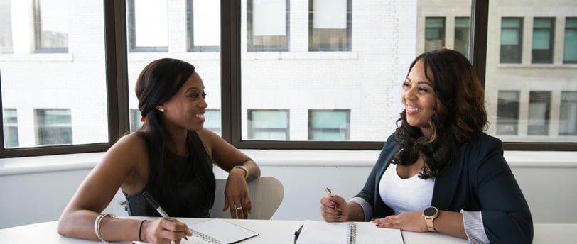 two women sitting at a table with notebooks and notebooks