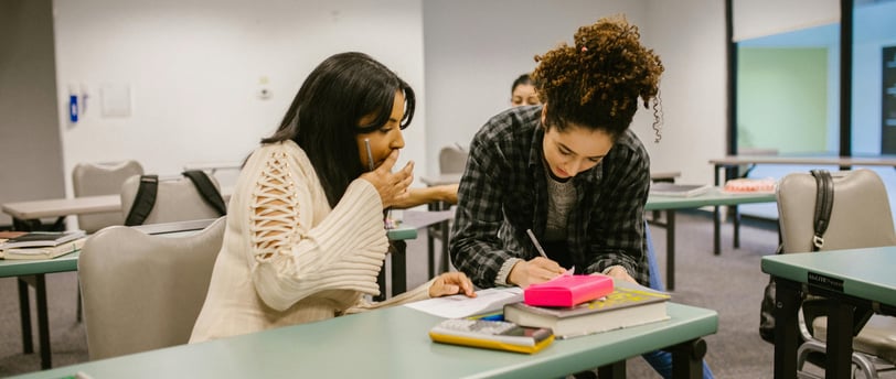 two woman sitting at desks in a classroom