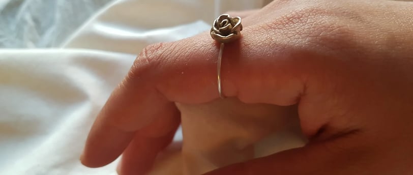 a person's hand holding a ring with a rose on it