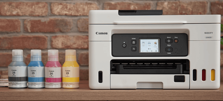 Canon MAXIFY GX4020 MegaTank Printer with four ink bottles on a wooden surface against a brick wall.