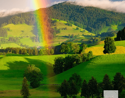 rainbow sur une campagne avec des champs verts vallonées et sous un ciel bleu et blanc